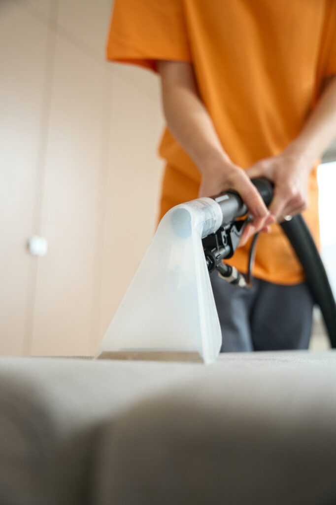 Worker from cleaning company performing general cleaning of sofa